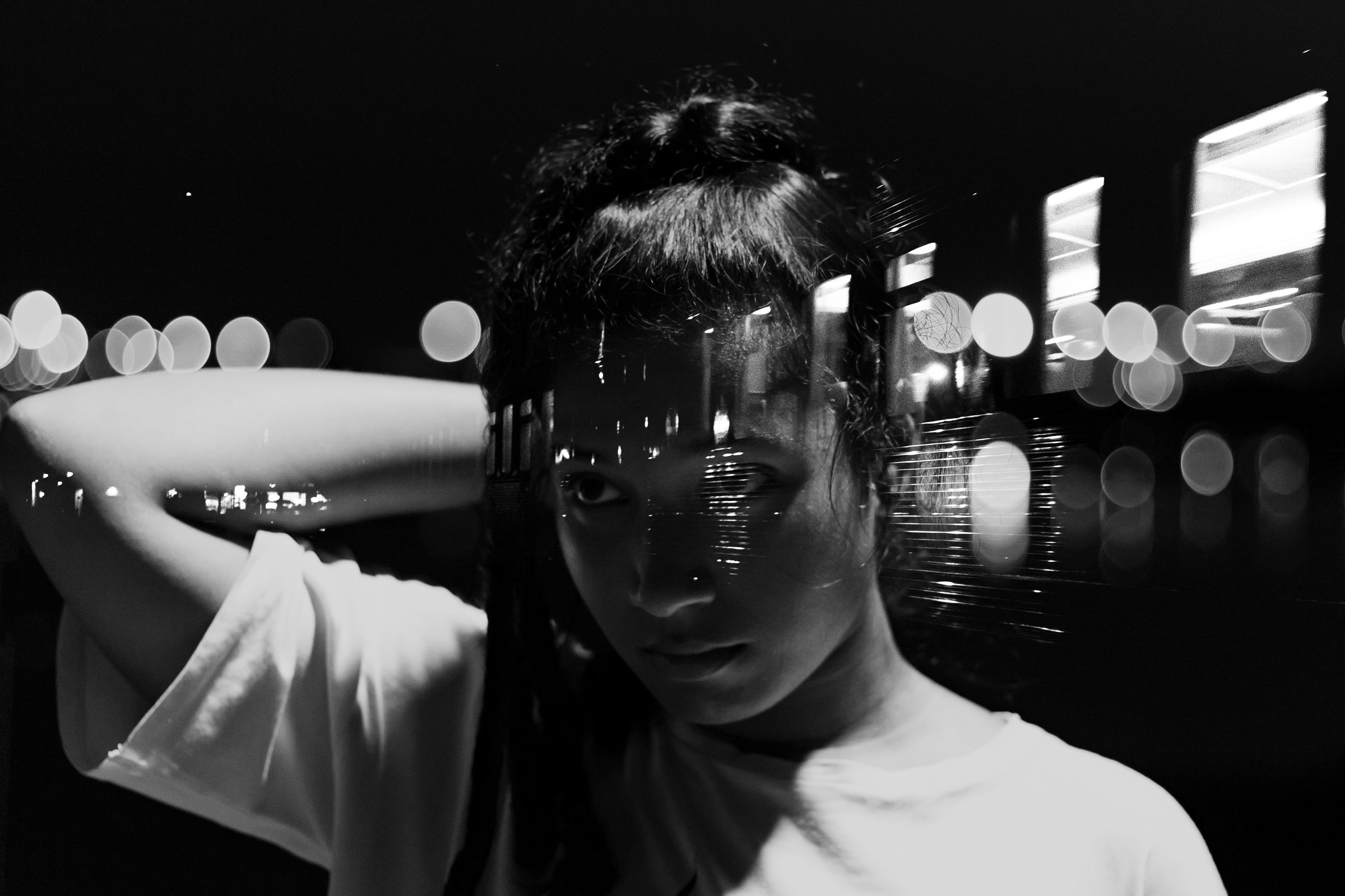 Retrato em preto e branco de uma jovem, com luzes da cidade refletidas